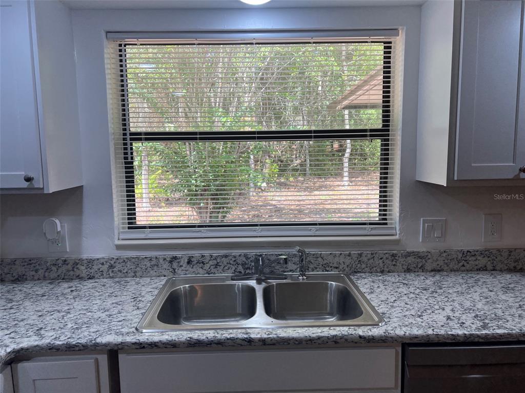 A kitchen sink with a granite countertop sits in front of a window with blinds — 9700 SW 209TH COURT, DUNNELLON, FL