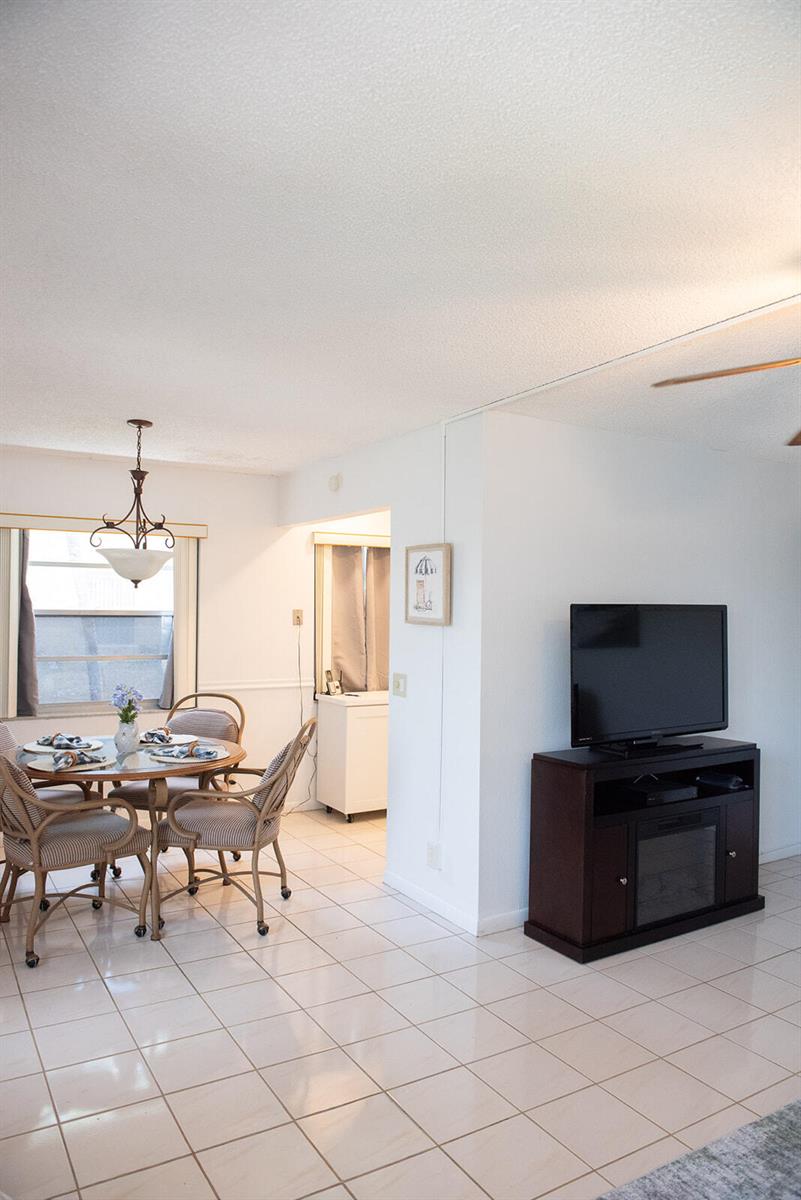 A dining area with a glass table and wicker chairs sits beside a television console — 416 Capri I, Delray Beach FL 33484, DELRAY BEACH, FL