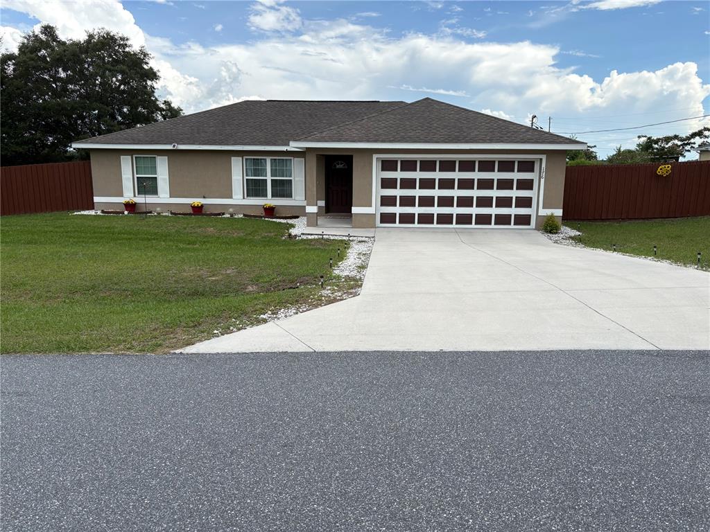 A single-story house with a tan stucco exterior, a two-car garage, and a red fence — 176 JUNIPER LOOP CIRCLE, OCALA, FL