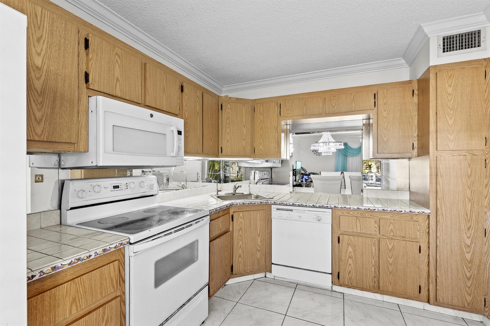 A kitchen features light oak cabinets, white appliances, tiled countertops, and a mirrored backsplash — 218 Foxtail Drive # B, FL 33415, FL