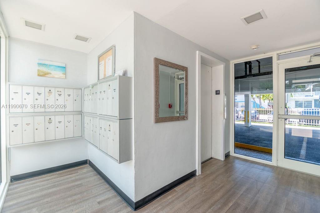 A building lobby features mailboxes, a mirror, and a glass door leading to a parking area — 1990 Marseille Dr # 402, Miami Beach FL 33141, MIAMI BEACH, FL