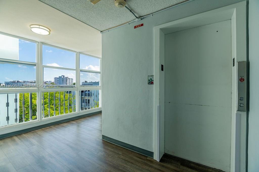 An elevator door is located in a hallway with wood-look flooring and large windows — 1990 Marseille Dr # 402, Miami Beach FL 33141, MIAMI BEACH, FL