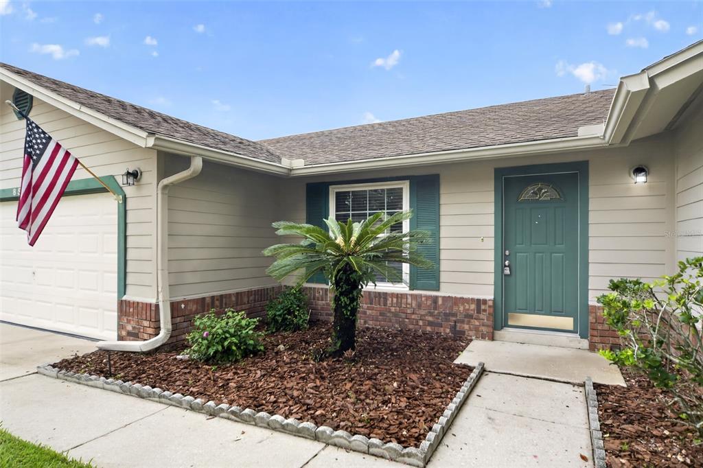 The exterior of a house features beige siding, a green front door, and a small palm — 854 N JERICO DRIVE, CASSELBERRY, FL