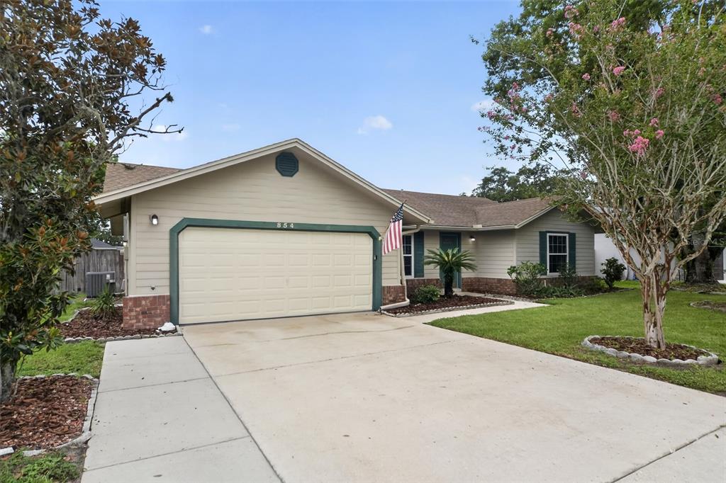 A single-story house with tan siding, a two-car garage, and a concrete driveway — 854 N JERICO DRIVE, CASSELBERRY, FL
