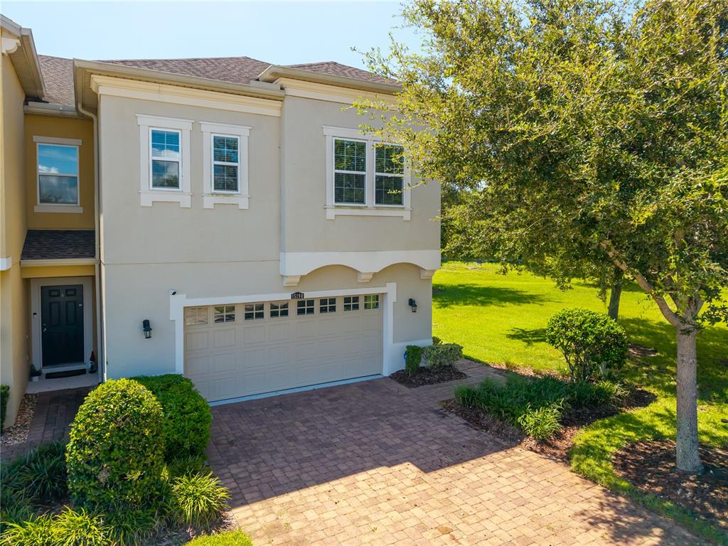 A two-story townhouse features a beige stucco exterior, a two-car garage, and a paved driveway — 15190 SUNRISE GROVE CT, WINTER GARDEN, FL
