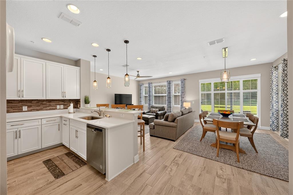 An open-concept kitchen, dining area, and living room featuring white cabinets and wood-look tile flooring — 15190 SUNRISE GROVE CT, WINTER GARDEN, FL