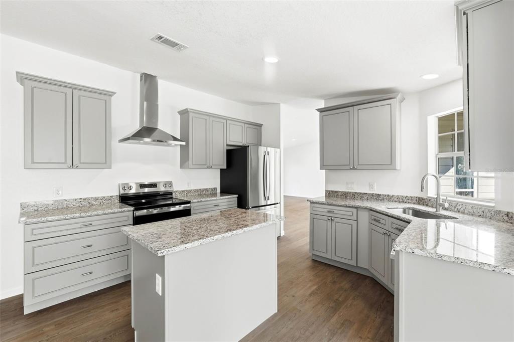 A kitchen features gray cabinets, granite countertops, stainless steel appliances, and wood-look flooring — 5180 LEXINGTON CIRCLE, WILDWOOD, FL