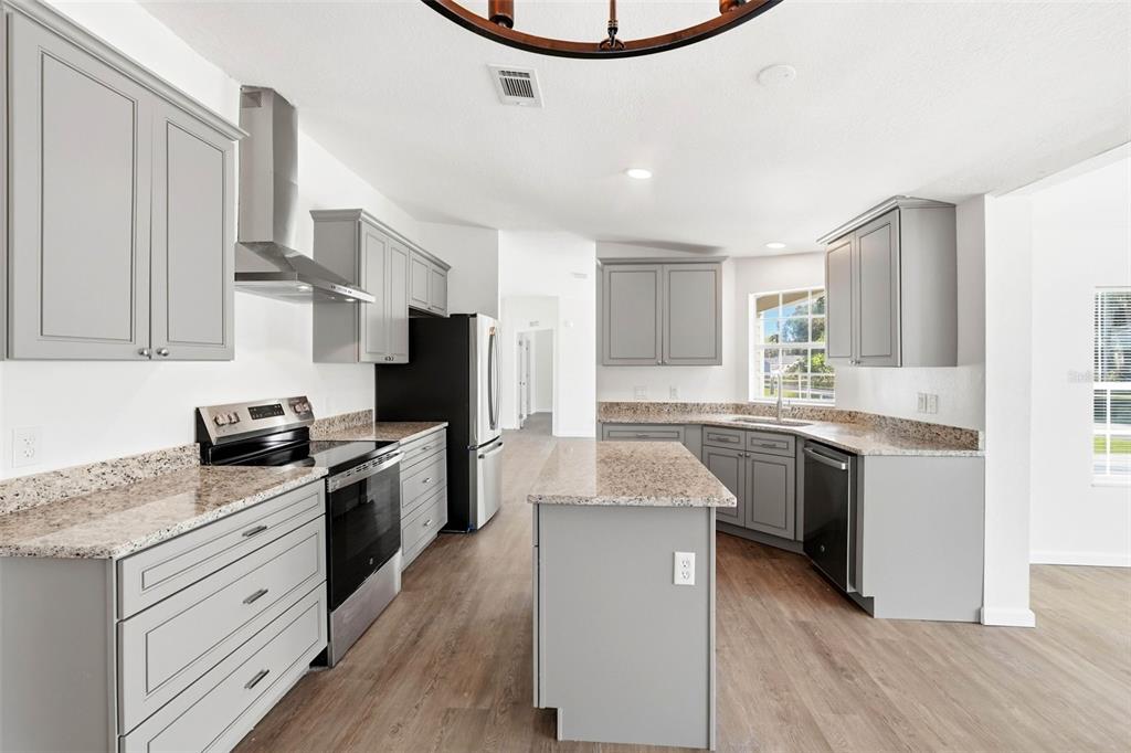 A kitchen with gray cabinets, granite countertops, stainless steel appliances, and wood-look flooring — 5180 LEXINGTON CIRCLE, WILDWOOD, FL