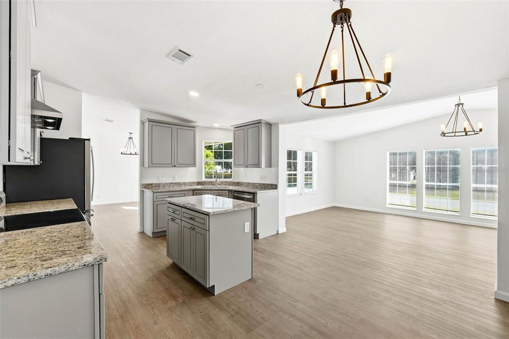 A kitchen with gray cabinets and granite countertops opens into a bright, spacious dining area — 5180 LEXINGTON CIRCLE, WILDWOOD, FL
