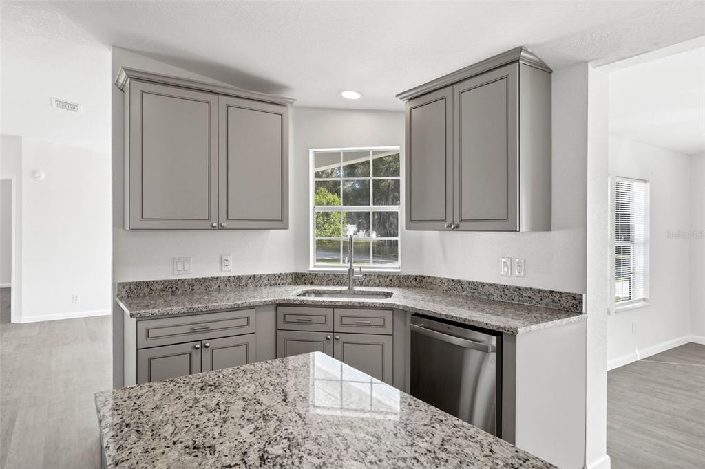 A kitchen features gray cabinets, granite countertops, a corner sink, and stainless steel appliances — 5180 LEXINGTON CIRCLE, WILDWOOD, FL