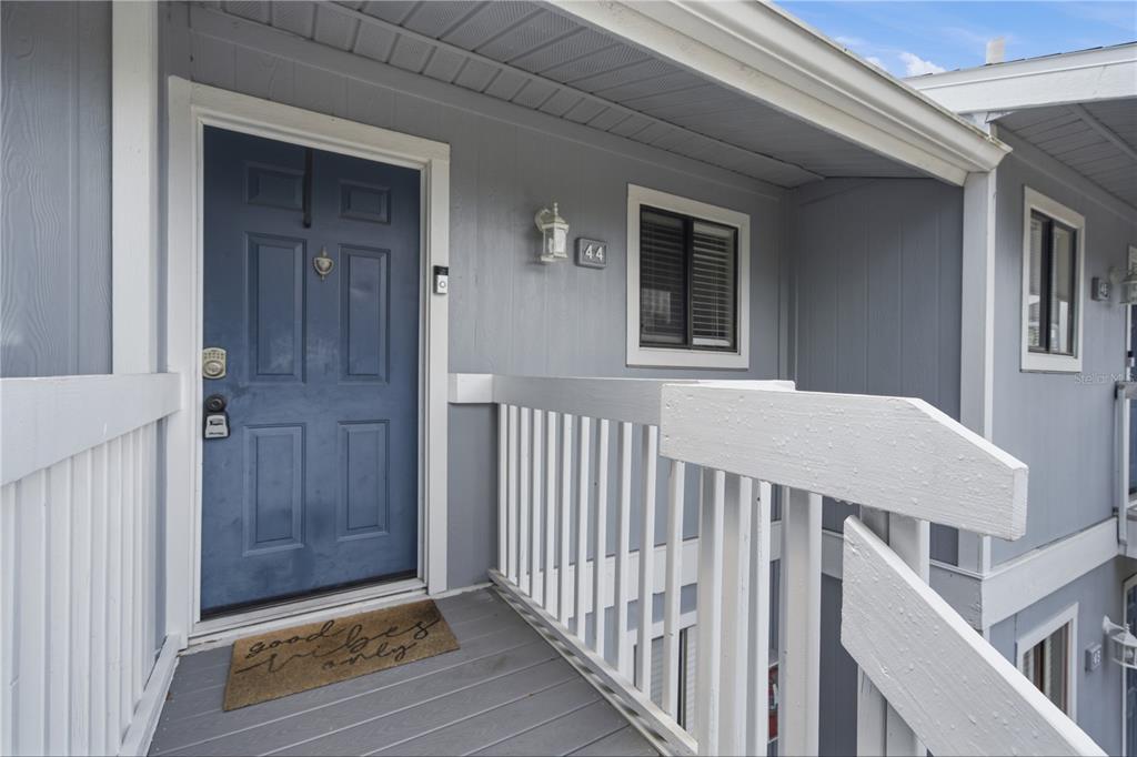 An exterior view of a blue front door with a welcome mat on a porch — 6033 34TH STREET W UNIT 44, BRADENTON, FL