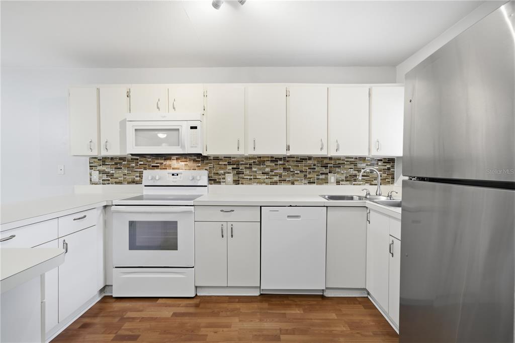 A kitchen features white cabinets, a tiled backsplash, white appliances, and a stainless steel refrigerator — 6033 34TH STREET W UNIT 44, BRADENTON, FL