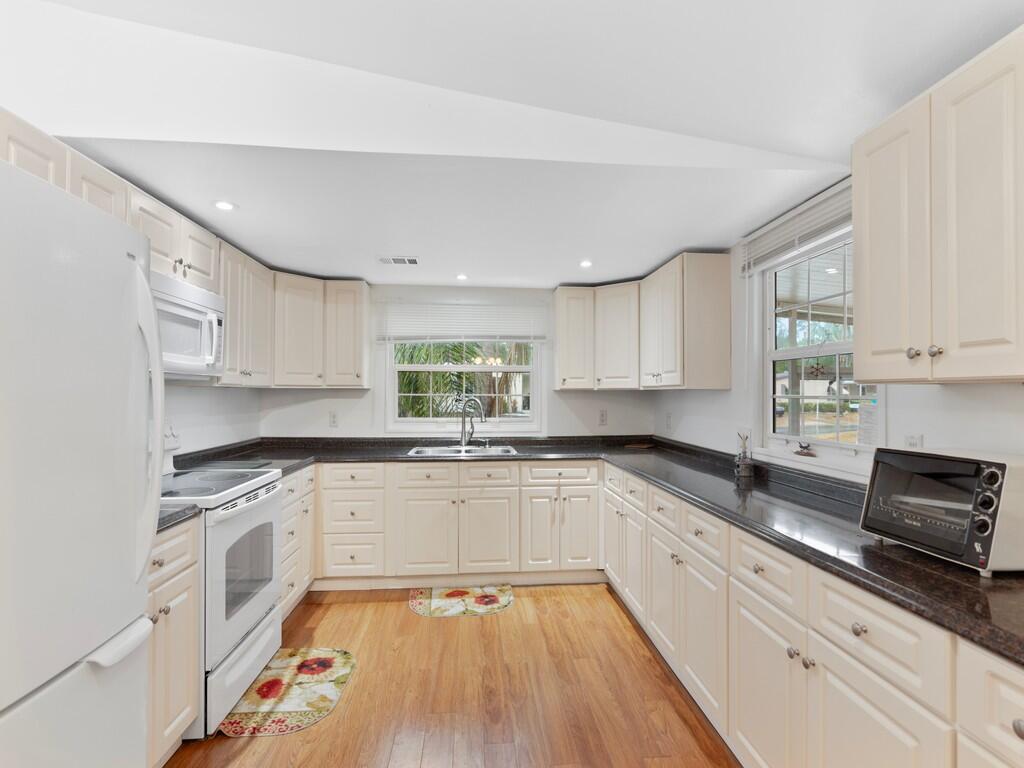 A kitchen with cream cabinets, dark countertops, white appliances, and wood-look flooring — 471 Tropical Isles Circle, Fort Pierce FL 34982, FORT PIERCE, FL