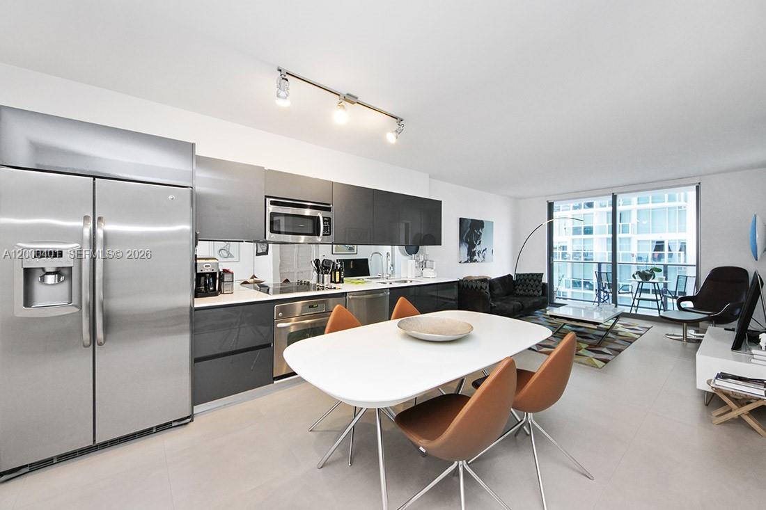 A modern open-concept kitchen and living area features gray cabinetry, stainless appliances, and a dining table — 31 SE 6th St # 1206, Miami FL 33131, MIAMI, FL