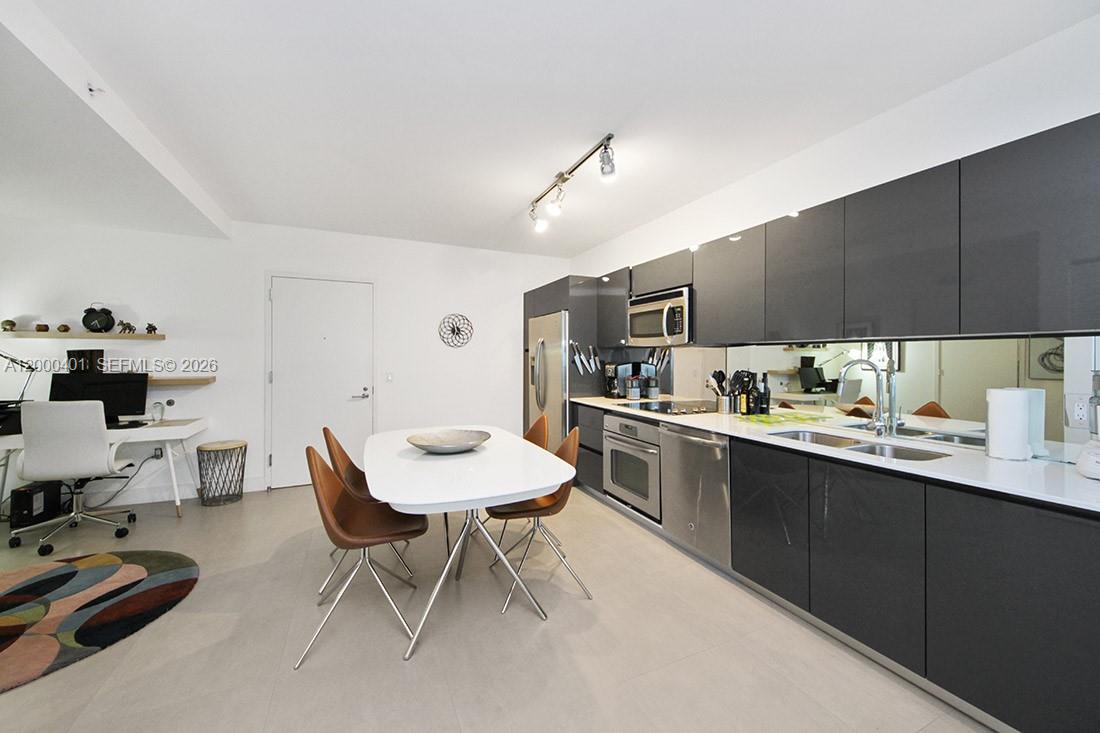 A modern kitchen features dark gray cabinetry, stainless steel appliances, and an adjacent dining area — 31 SE 6th St # 1206, Miami FL 33131, MIAMI, FL