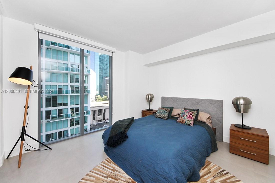 A bedroom features a blue bed, two nightstands, a floor lamp, and floor-to-ceiling windows — 31 SE 6th St # 1206, Miami FL 33131, MIAMI, FL