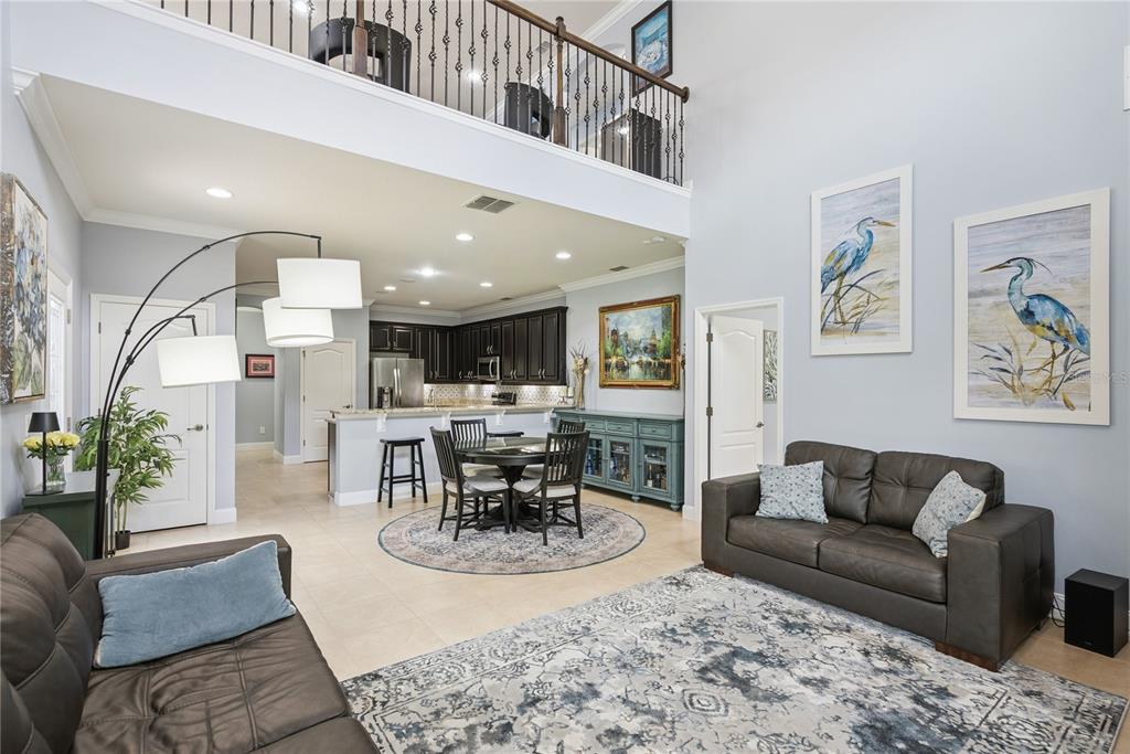 An open-concept living and dining area features dark leather sofas, a kitchen, and a loft — 5571 SIRACUSA LANE, SANFORD, FL