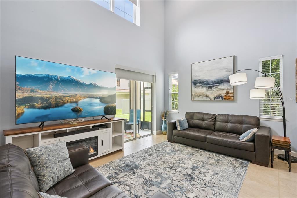 A living room features a large television, a fireplace console, and a dark leather sofa — 5571 SIRACUSA LANE, SANFORD, FL
