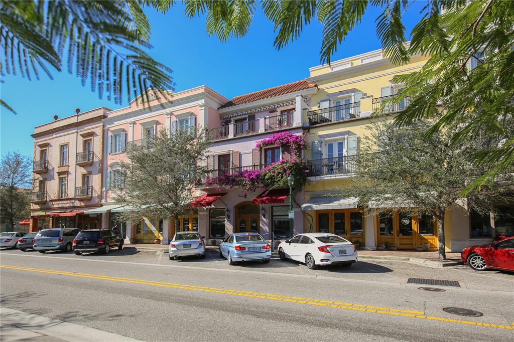 A street-level view of a multi-story building with storefronts, balconies, and parked cars — 430 KUMQUAT COURT UNIT 406, SARASOTA, FL