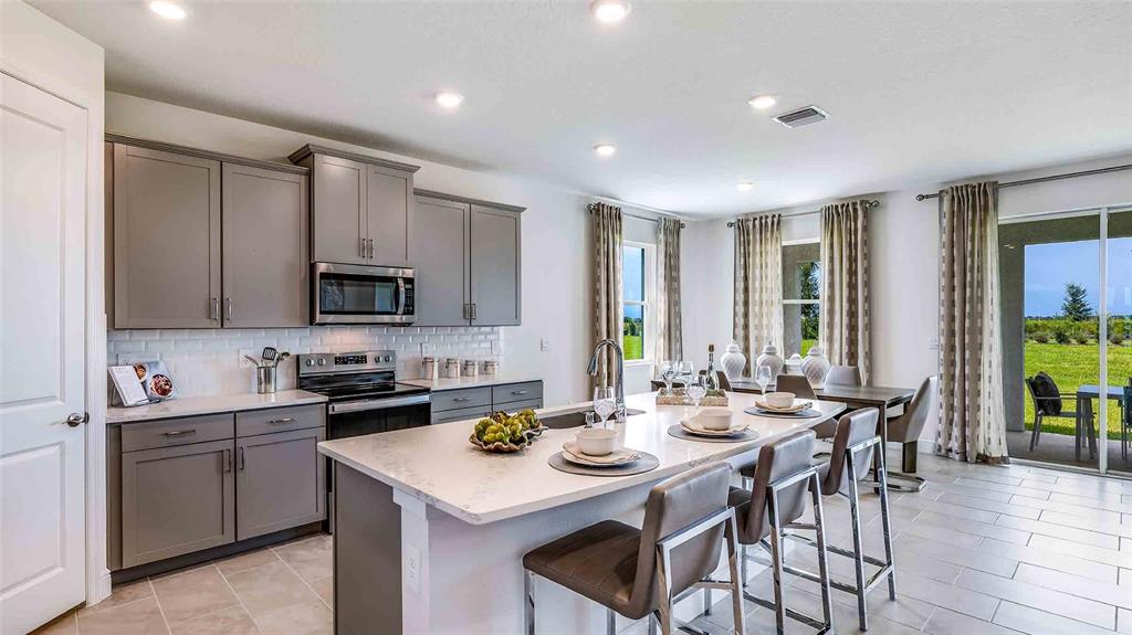 A kitchen with gray cabinets, a white island, and a dining area overlooking a yard — 18245 GANDER TERRACE, LAKEWOOD RANCH, FL