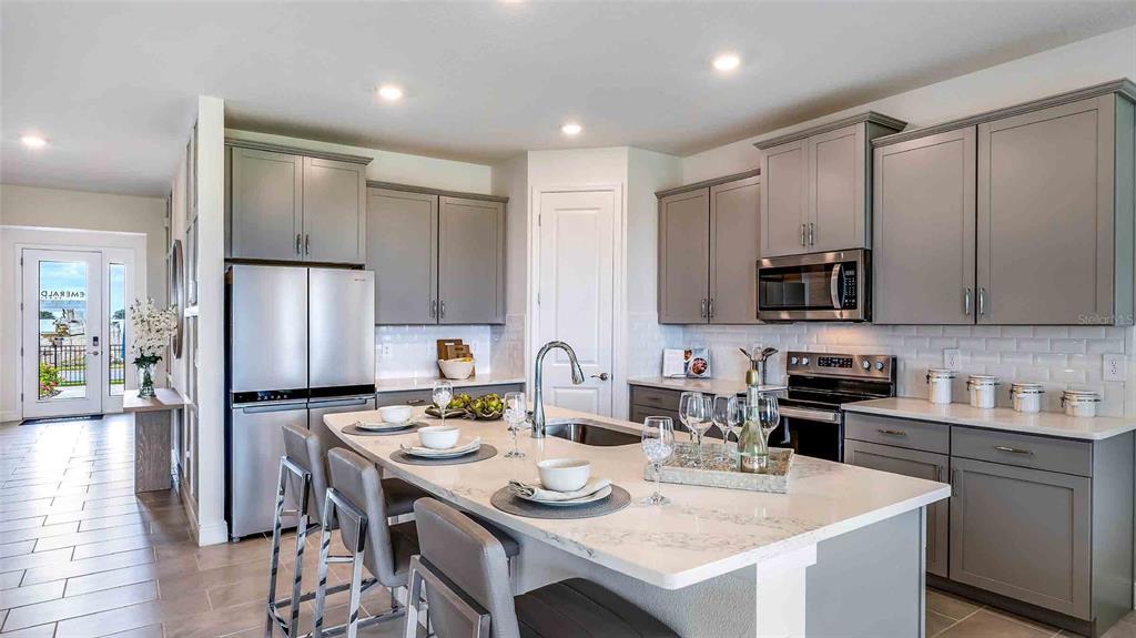 A modern kitchen features gray cabinetry, a white quartz island, and stainless steel appliances — 18245 GANDER TERRACE, LAKEWOOD RANCH, FL