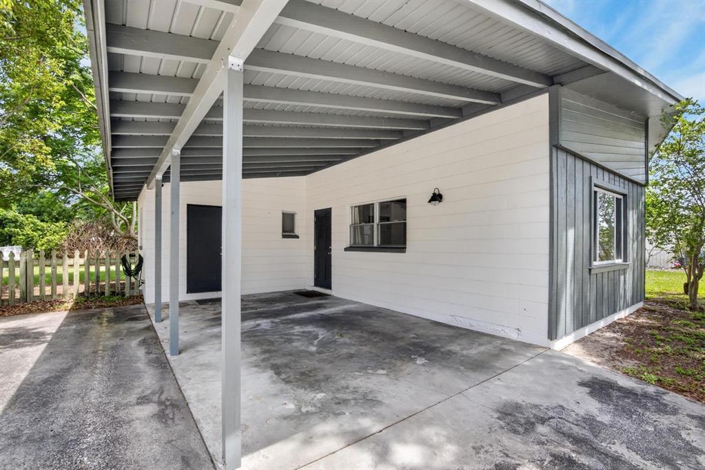 A concrete carport with a gray metal roof attached to a white-walled house exterior — 113 6TH JPV STREET, WINTER HAVEN, FL