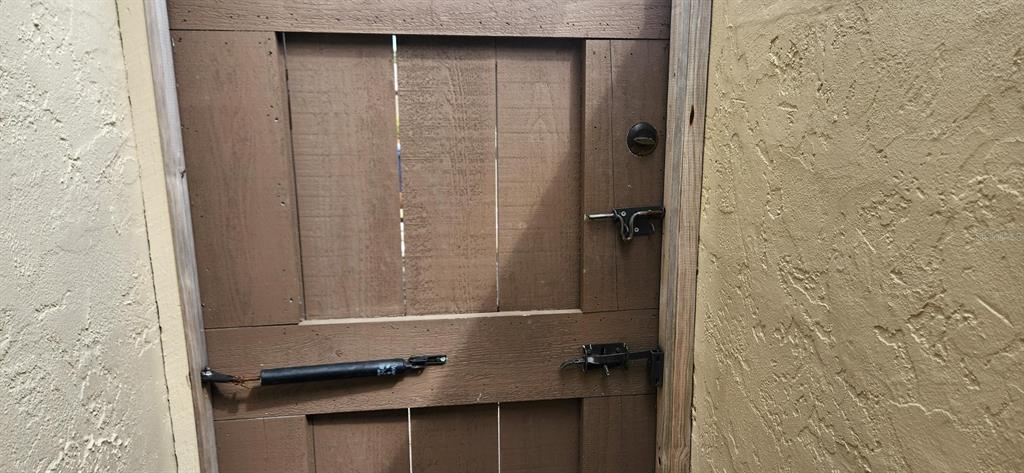 A wooden gate with a metal latch and a hydraulic closer is set between stucco walls — 3466 BEEKMAN PLACE UNIT 36, SARASOTA, FL