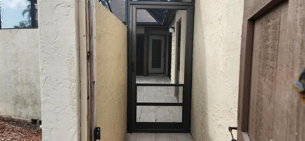 A metal screen door leads to a paved entryway between two stucco exterior walls — 3466 BEEKMAN PLACE UNIT 36, SARASOTA, FL