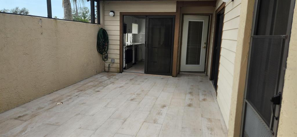 A tiled patio area features a sliding glass door, a side door, and a wall-mounted hose — 3466 BEEKMAN PLACE UNIT 36, SARASOTA, FL