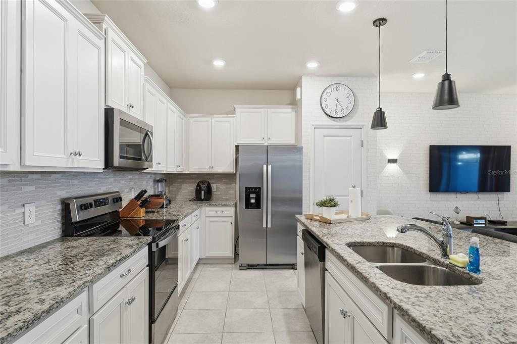 A modern kitchen features white cabinets, granite countertops, stainless steel appliances, and a central island — 236 JETTY WAY, DAVENPORT, FL