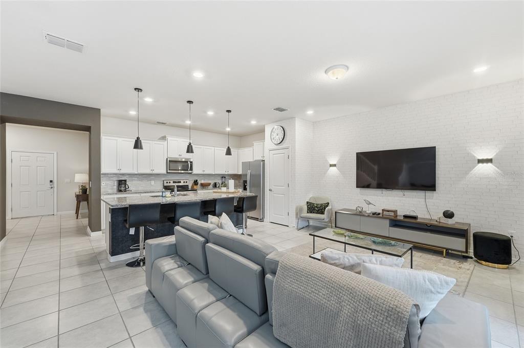 An open-concept living room and kitchen featuring white brick walls, tile flooring, and gray furniture — 236 JETTY WAY, DAVENPORT, FL