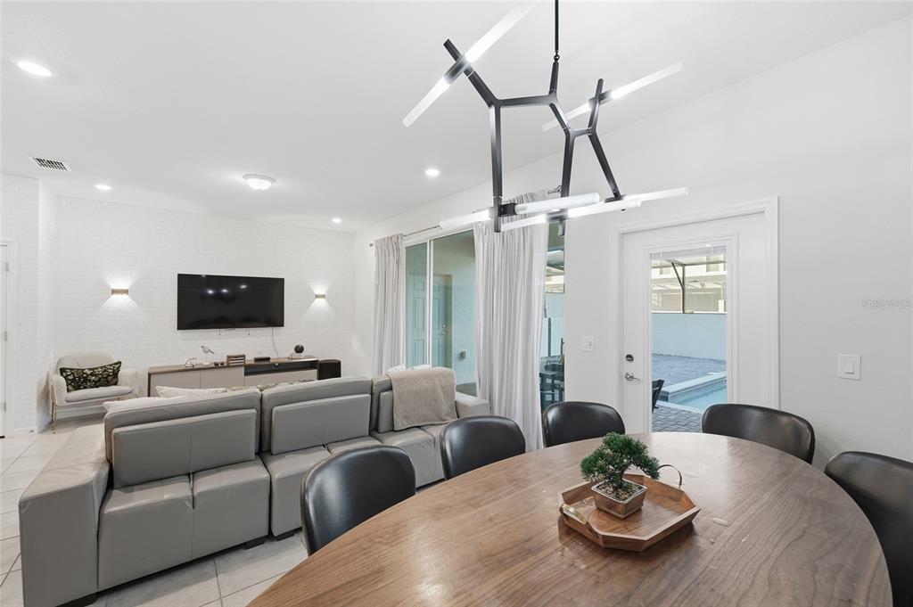 A living and dining area features a grey sectional sofa, wooden table, and modern chandelier — 236 JETTY WAY, DAVENPORT, FL