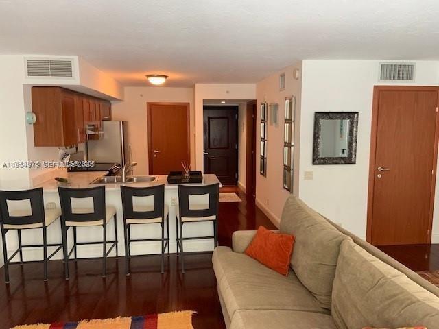 A kitchen with a breakfast bar and stools overlooks a living area with a sofa — 9499 Collins Ave # 205, Surfside FL 33154, SURFSIDE, FL