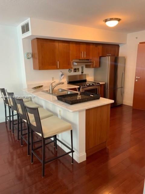 A kitchen features wood cabinets, stainless steel appliances, a breakfast bar, and hardwood floors — 9499 Collins Ave # 205, Surfside FL 33154, SURFSIDE, FL