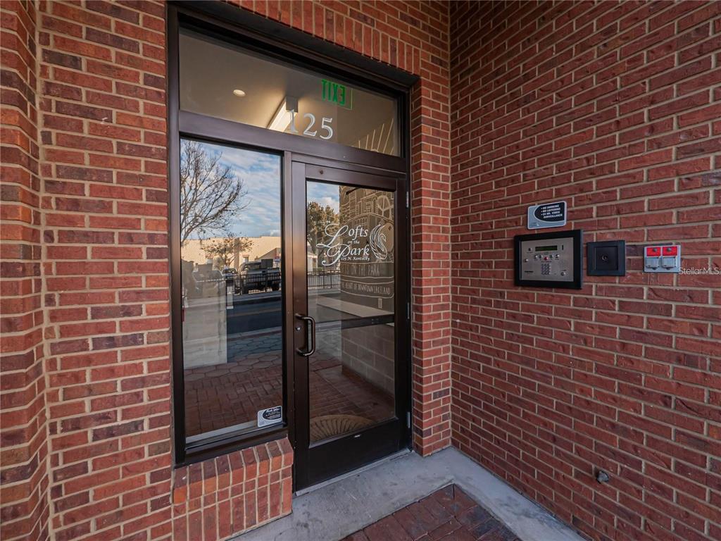 A glass door with a metal frame is set into a red brick exterior wall — 125 N KENTUCKY AVENUE UNIT 203, LAKELAND, FL