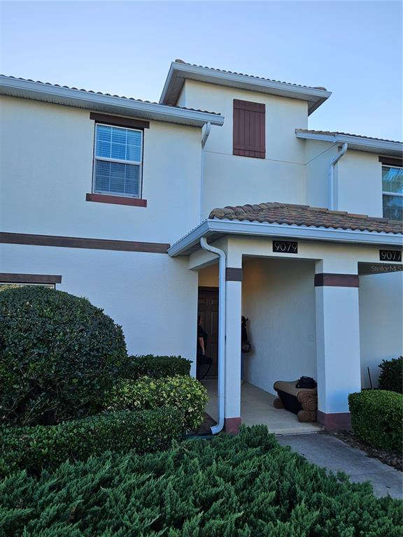 The exterior of a two-story stucco townhouse features a covered entryway and a small bench — 9079 DOGLEG DRIVE, DAVENPORT, FL