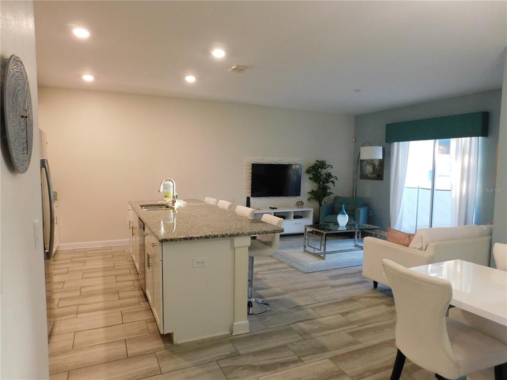 An open-concept kitchen with a granite island overlooks a living area with tile flooring — 9079 DOGLEG DRIVE, DAVENPORT, FL