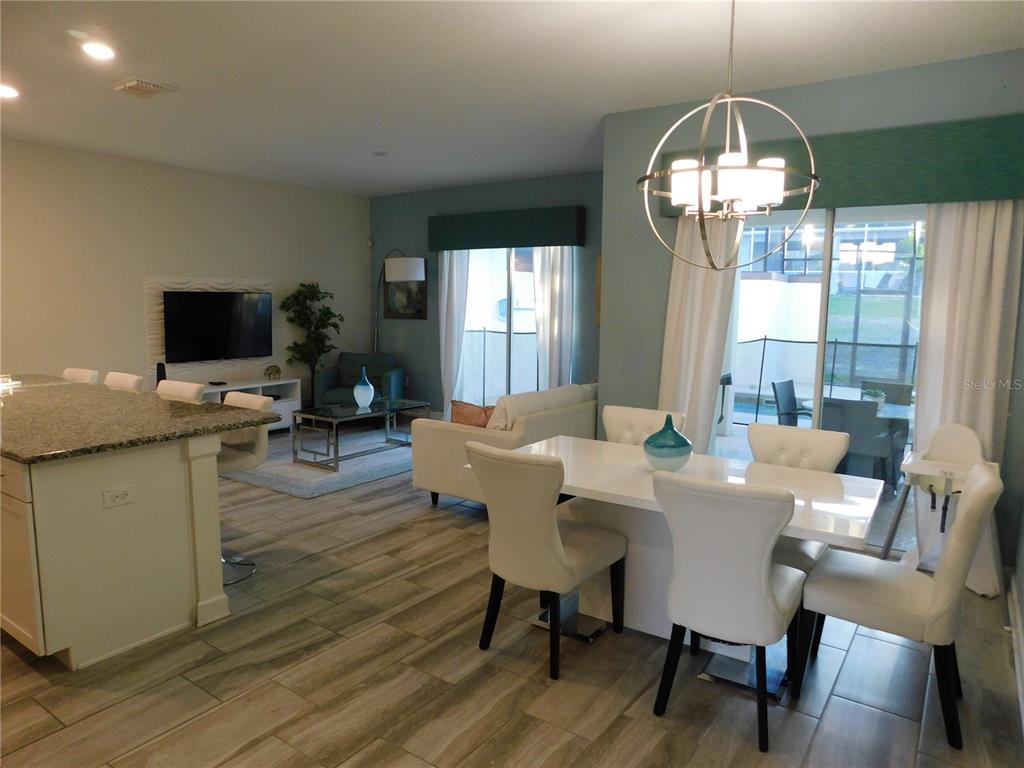 An open-concept living and dining area features tile flooring, a kitchen island, and modern lighting — 9079 DOGLEG DRIVE, DAVENPORT, FL