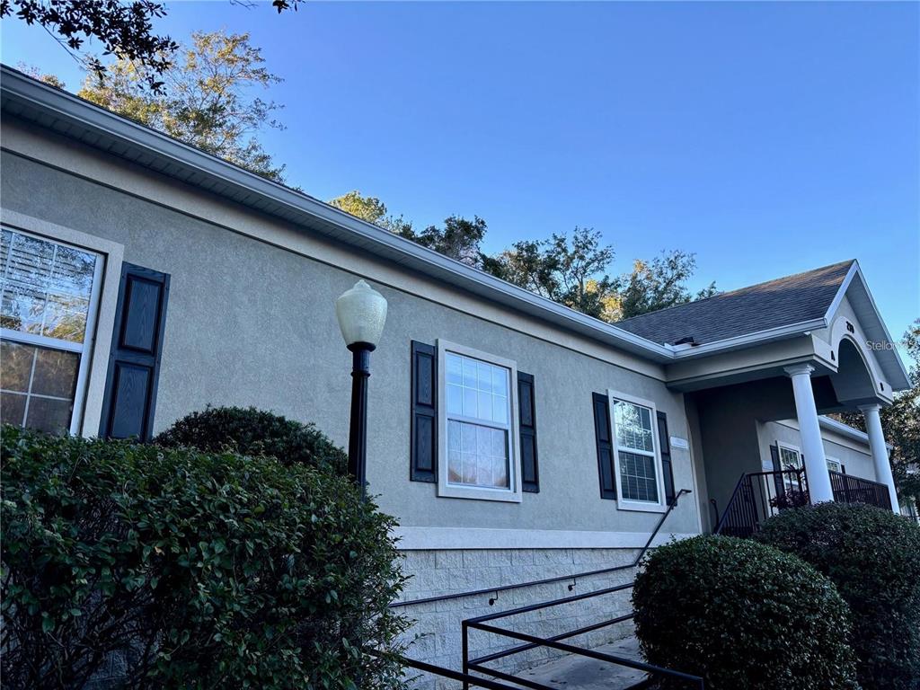 A low-angle exterior view of a building with stucco walls, dark shutters, and a ramp — 230 NW 76TH DRIVE UNIT B, GAINESVILLE, FL