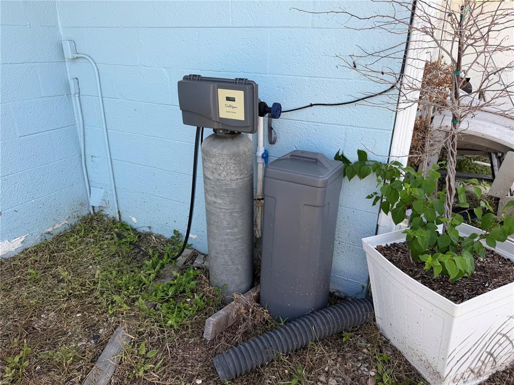 A Culligan water softener system sits against the exterior blue wall of a house — 318 SKYLARK LANE NW, PORT CHARLOTTE, FL