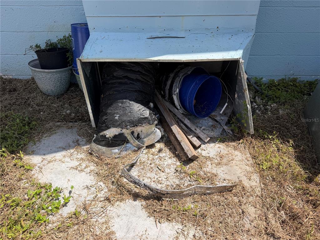 An outdoor metal enclosure contains a damaged flexible duct, wooden boards, and a blue bucket — 318 SKYLARK LANE NW, PORT CHARLOTTE, FL