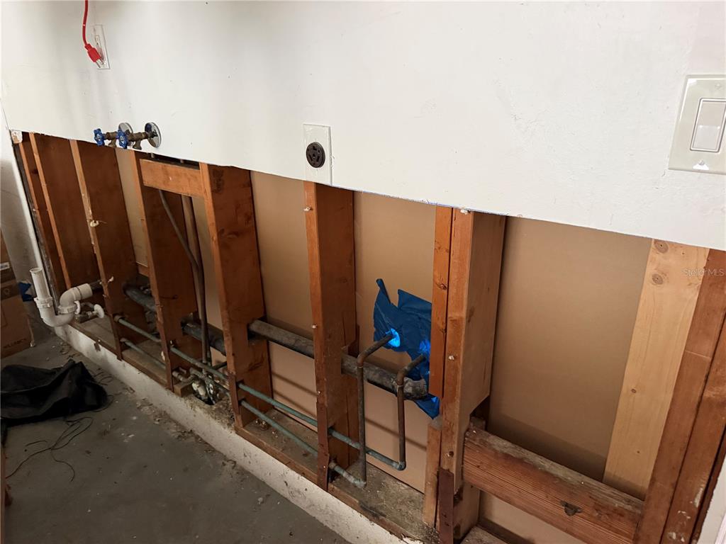 An unfinished wall with exposed wooden studs and plumbing pipes in a utility area — 318 SKYLARK LANE NW, PORT CHARLOTTE, FL