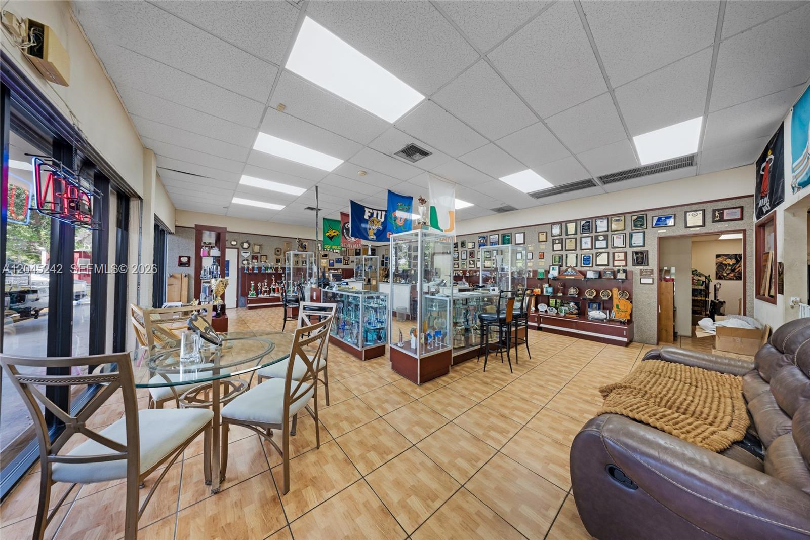 A commercial space features a glass table, display cases, numerous wall-mounted awards, and tile flooring — 9465 SW 56th St, Miami FL 33165, MIAMI, FL