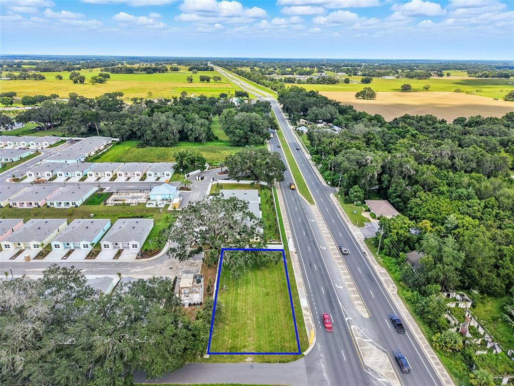 An aerial view shows a rectangular vacant lot outlined in blue next to a highway — 12182 N US HIGHWAY 301, OXFORD, FL