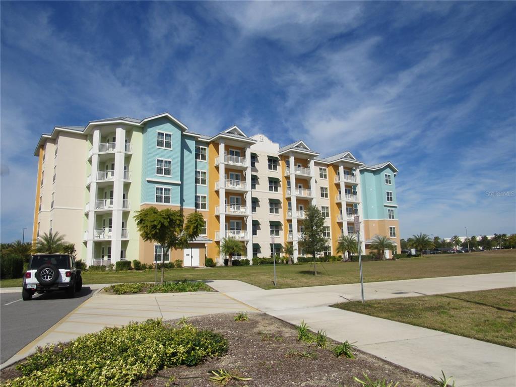 A multi-story apartment building with colorful exterior walls stands next to a paved parking lot — 3151 SUNSET WALK DR UNIT 1104, KISSIMMEE, FL