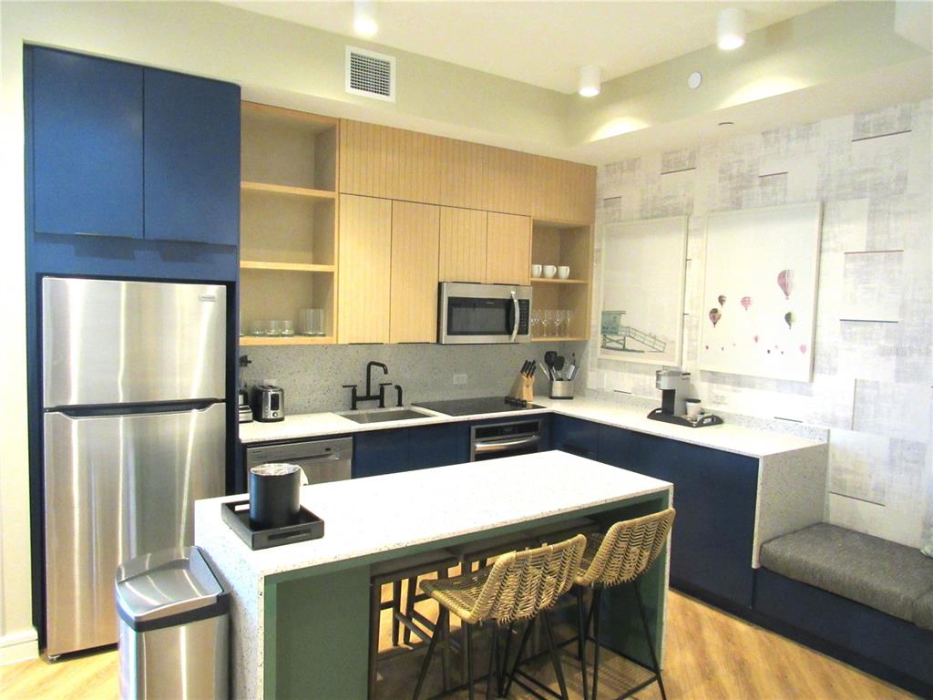 A modern kitchen features blue and wood cabinetry, a white island, and a built-in bench — 3151 SUNSET WALK DR UNIT 1104, KISSIMMEE, FL