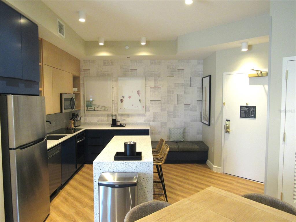 A modern kitchen features dark blue cabinets, a speckled island, and a built-in bench seat — 3151 SUNSET WALK DR UNIT 1104, KISSIMMEE, FL