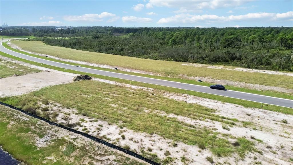 An aerial view shows a paved road winding through a large, undeveloped grassy lot — 6123 SOLSTICE DRIVE, TITUSVILLE, FL