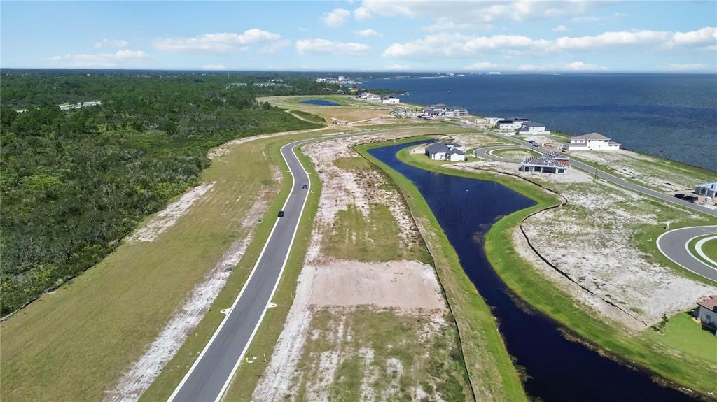 An aerial view shows a coastal residential development with a road, pond, and vacant lots — 6123 SOLSTICE DRIVE, TITUSVILLE, FL