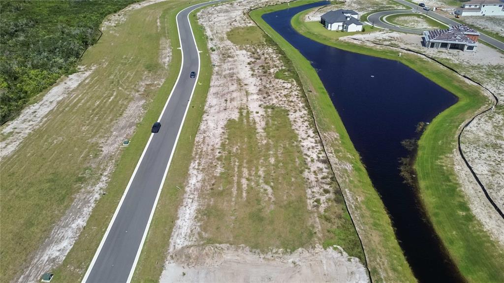 An aerial view shows a vacant residential lot situated between a curved road and a pond — 6123 SOLSTICE DRIVE, TITUSVILLE, FL
